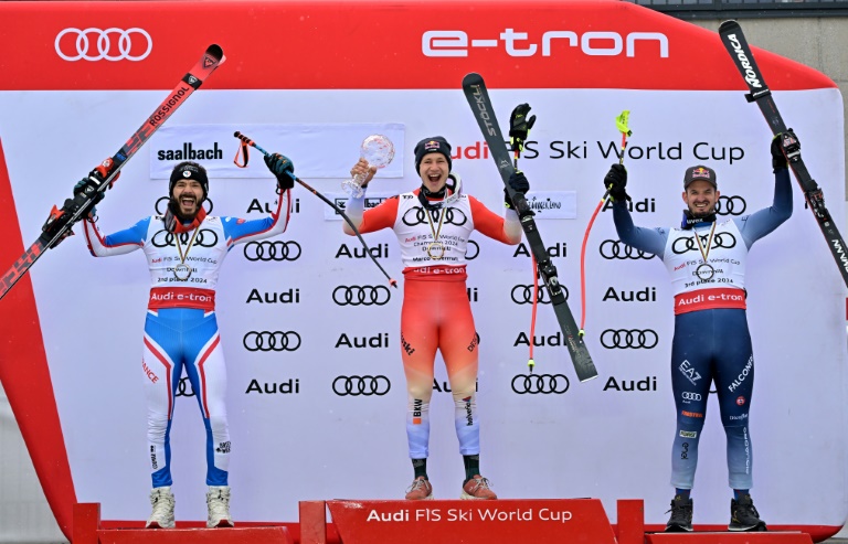Le podium de la Coupe du monde de descente avec le Français Cyprien Sarrazin (g) et l'Italien Dominik Paris (d) entourant le vainqueur, le Suisse Marco Odermatt, le 24 mars 2024 à Saalbach (Autriche)