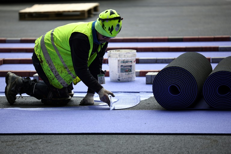 Un ouvrier pose des pistes d'athlétisme violettes pendant les travaux de rénovation pour adapter le Stade de France en vue des Jeux olympiques de Paris 2024, à Saint-Denis, en banlieue parisienne, le 9 avril 2024
