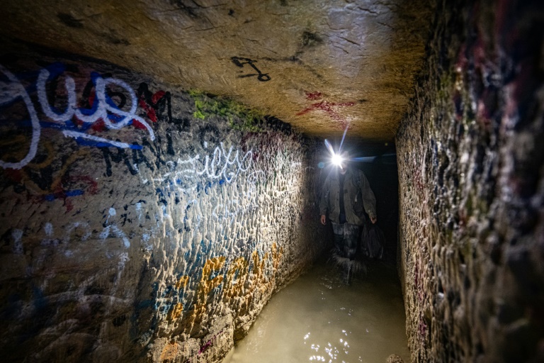 Un cataphile, lampe frontale sur la tête, avance les pieds dans l'eau dans les carrières souterraines de Paris, le 20 avril 2024