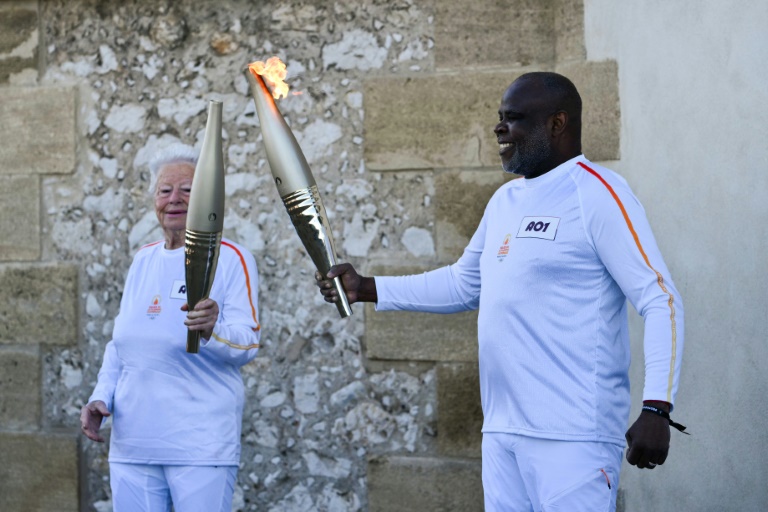L'ancien footballeur français Basile Boli (d) allume le flambeau de Colette Cataldo, supportrice historique de l’OM dans le cadre des relais de la flamme olympique et paralympique à la basilique Notre Dame de la Garde, à Marseille, le 9 mai 202
