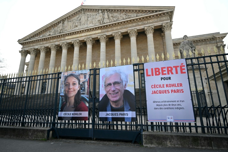 Les portraits de Cécile Kohler (G) et de Jacques Paris (C) exposés sur les grilles du Palais Bourbon, siège de l'Assemblée nationale française à Paris, le 25 mars 2025