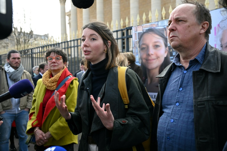 La soeur de Cécile Kohler, Noémie Kohler (C), entourée par ses parents Mireille (G) et Pascal Kohler (D), le 25 mars 2025 devant l'Assemblée nationale à Paris