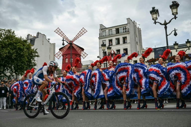 Le Français Valentin Madouas passe devant les danseuses du cabaret du Moulin Rouge à Montmartre lors de la course en ligne hommes des Jeux olympiques de Paris le 3 août 2024