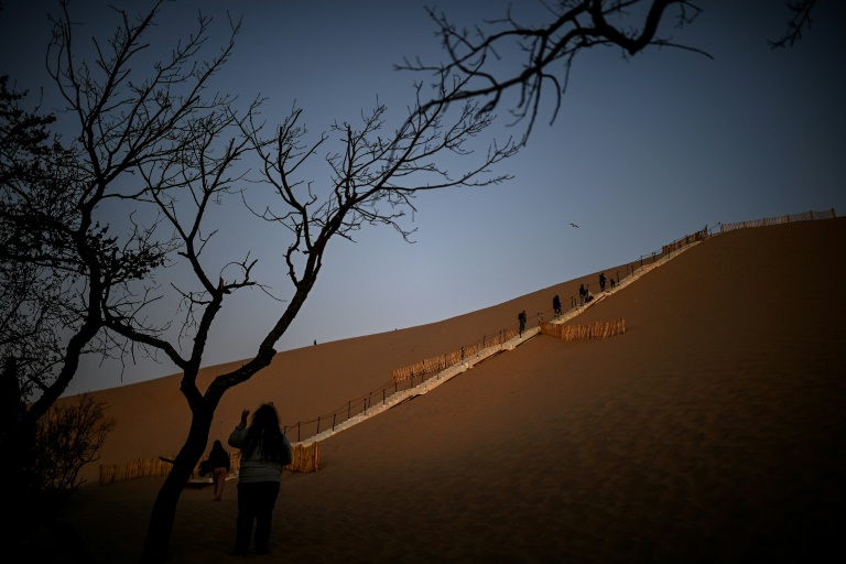 Des visiteurs utilisent les escaliers, au lever du soleil, pour gravir la dune du Pilat, le 10 avril 2025 à La Teste-de-Buch, en Gironde