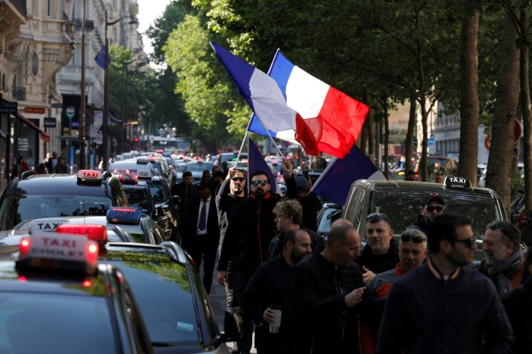 Des chauffeurs de taxi brandissent un drapeau français lors d'un rassemblement pour protester contre les nouvelles conditions tarifaires du transport sanitaires et la concurrence des VTC, à Paris, le 19 mai 2025