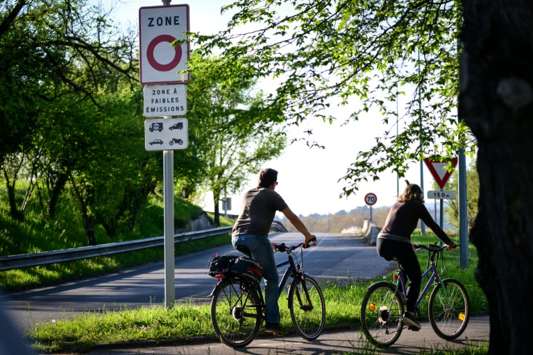 Des cyclistes passent à côté d'un panneau de zone à faibles émissions, le 5 avril 2025 à Lyon