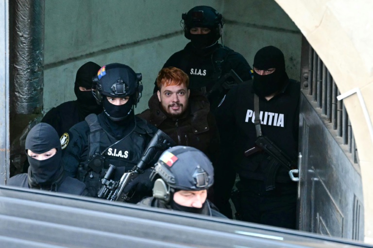 Mohamed Amra (c) escorté par des policiers, le 23 février 2025 à Bucarest, en Roumanie