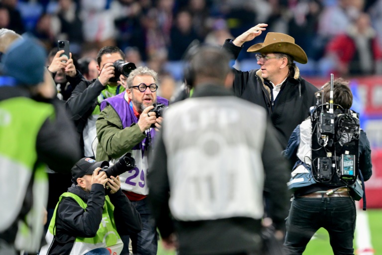 John Textor, chapeau sur la tête, entouré de journalistes le 23 février 2025 avant le match de L1 entre l'OL et le Paris SG au Groupama Stadium