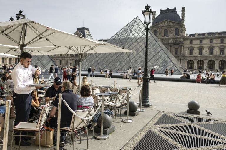 Un serveur sur une terrasse de restaurant près de la Pyramide du Louvre, conçue par l'architecte sino-américain Ieoh Ming Pei, au musée du Louvre, l'un des lieux qui sera rafraîchi avec l'eau de la Seine