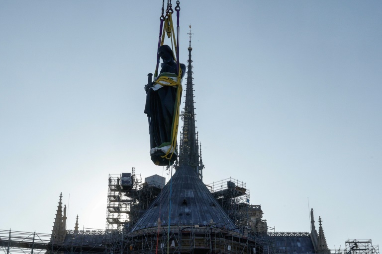 Une grue soulève l'une des 16 statues géantes d'apôtres pour la replacer sur sa base au pied de la flèche de la cathédrale Notre-Dame de Paris, le 23 juin 2025