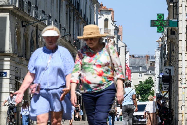 Des passants marchent dans une rue de Nantes alors qu'un thermomètre de pharmacie affiche 36 degrés, le 19 juin 2025