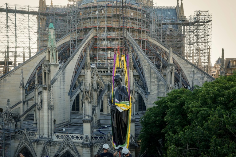 Une grue soulève l'une des 16 statues géantes d'apôtres pour la replacer sur sa base au pied de la flèche de la cathédrale Notre-Dame de Paris, le 23 juin 2025