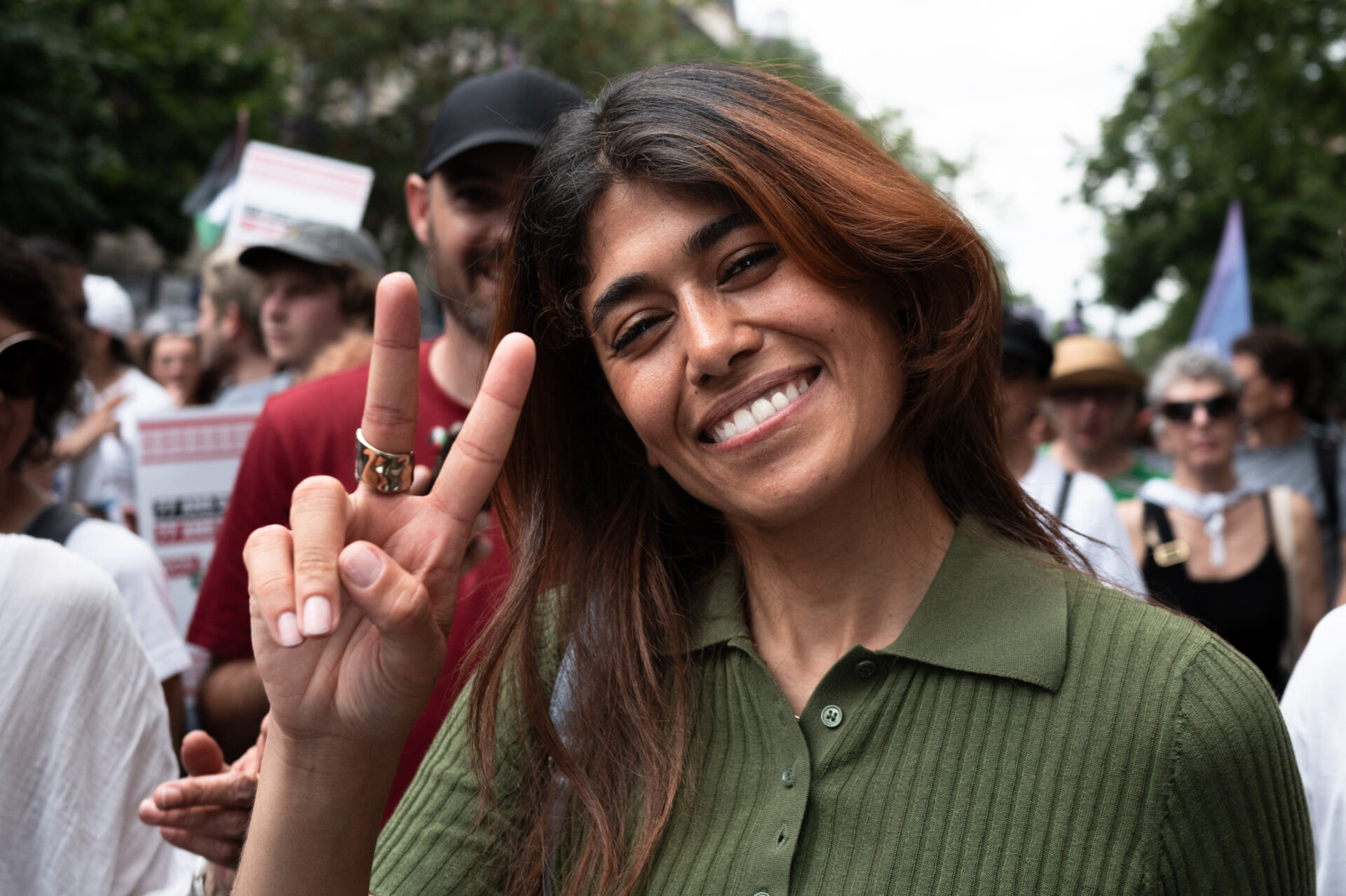 Rima Hassan pose devant l'objectif avec un grand sourire et en faisant le signe "V" avec sa main