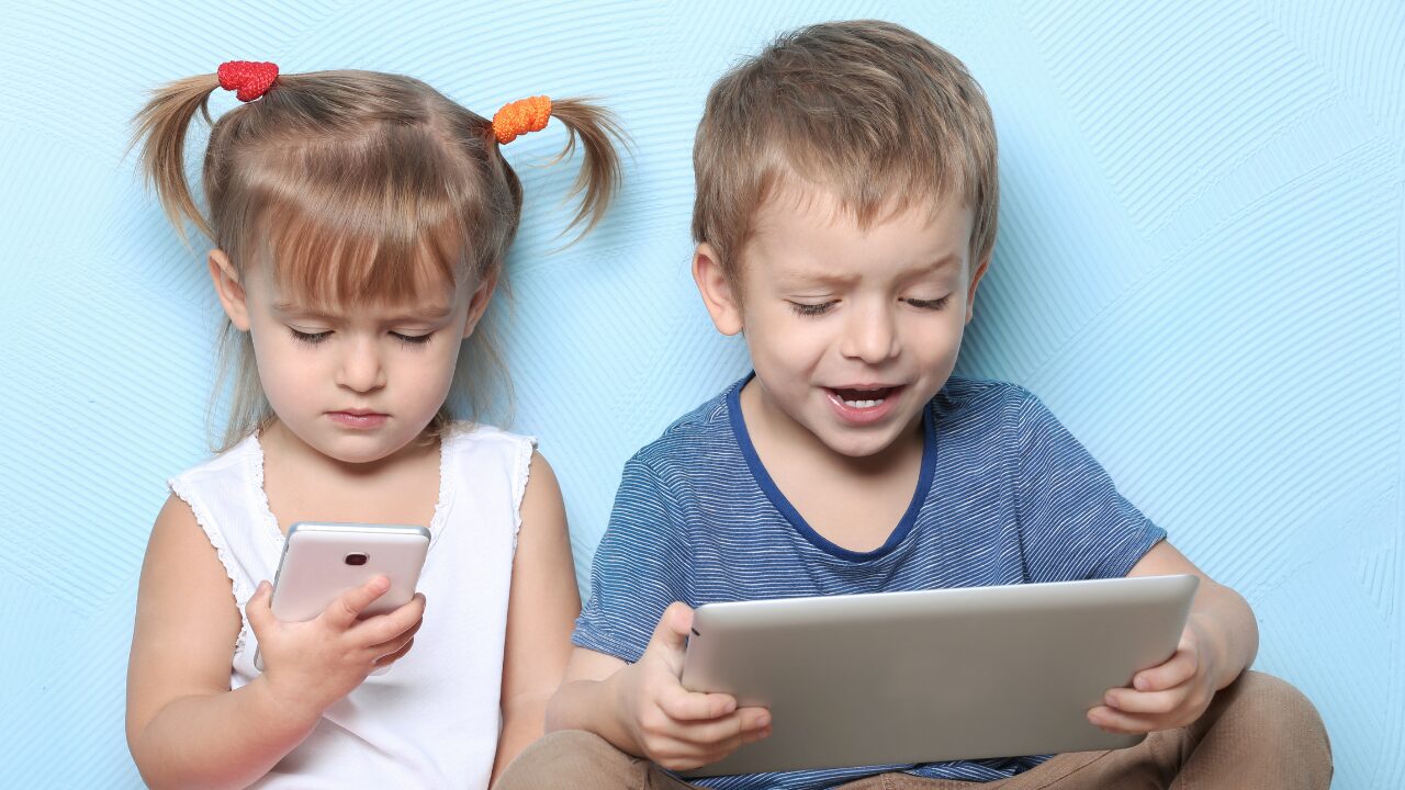 Deux enfants tiennent dans leurs mains une tablette et un téléphone portable, qu'ils regardent fixement