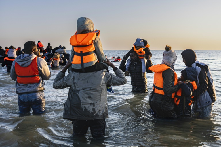Des migrants avancent dans l'eau pour embarquer sur le bateau d'un passeur et tenter de traverser la Manche au large de la plage de Gravelines, le 16 juin 2025 dans le Nord