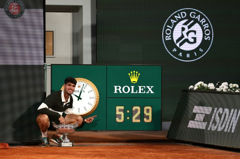 Carlos Alcaraz pose avec le trophée de Roland-Garros devant l'horloge indiquant la durée (5h29) de la finale contre Jannik Sinner, la plus longue de l'histoire du tournoi, le 8 juin 2025 à Paris