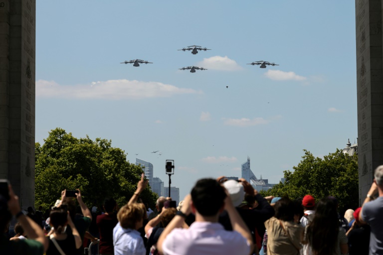 Des passants prennent des photos d'Airbus A400M de l'Armée de l'air française survolant l'Arc de Triomphe, le 9 juillet 2025 à Paris, lors d'une répétition du défilé annuel du 14 juillet