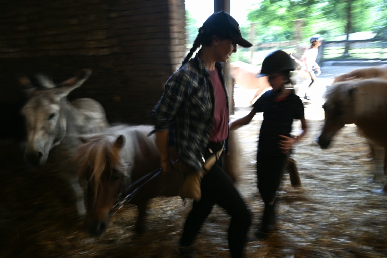 Agathe de Pas, qui a repris avec deux de ses frères la ferme équestre de Bois Guilbert, en Seine-Maritime, aide des enfants à guider leur poney, le 1er juillet 2025
