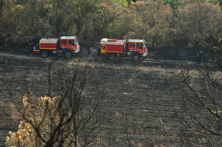 Des camions de pompiers évoluent sur un chemin dans une forêt touchée par des incendies, le 8 août 2025 à Lagrasse, dans l'Aude