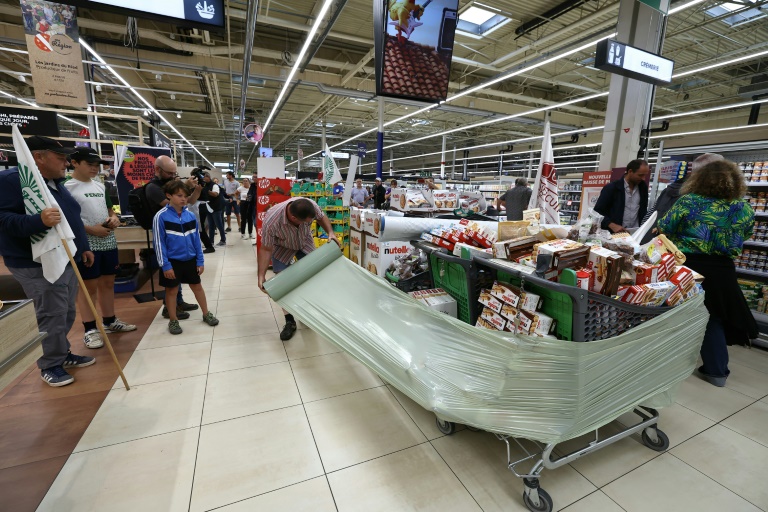 Des membres des syndicats agricoles FDSEA 72 et Jeunes Agriculteurs (JA) enveloppent des produits des produits contenant de l'acétamipride, un pesticide néonicotinoïde, retirés des rayons lors d'une opération de protestation dans un supermarché de Mundolsheim, le 20 août 2025 dans le Bas-Rhin
