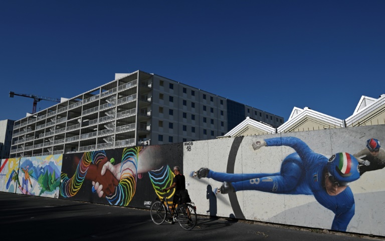Un cycliste passe devant le site de construction du Village olympique des Jeux de Milan-Cortina 2026  à Milan le 31 juillet 2025.