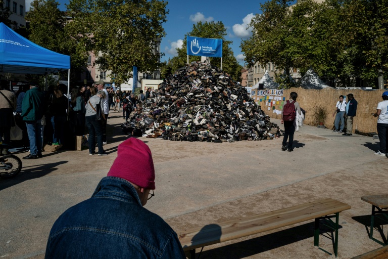 Des personnes autour d'une pyramide de chaussures organisée par Handicap international (HI) contre les mines antipersonnel, le 27 septembre 2025 à Lyon