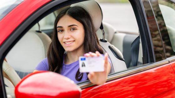 Young woman showing driving license while sitting in a red car (photology2000)
