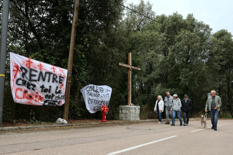 Des banderoles à côté d'une croix en bois objet de polémiques à l'entrée du village de Quasquara, le 14 octobre 2025 en Corse-du-Sud
