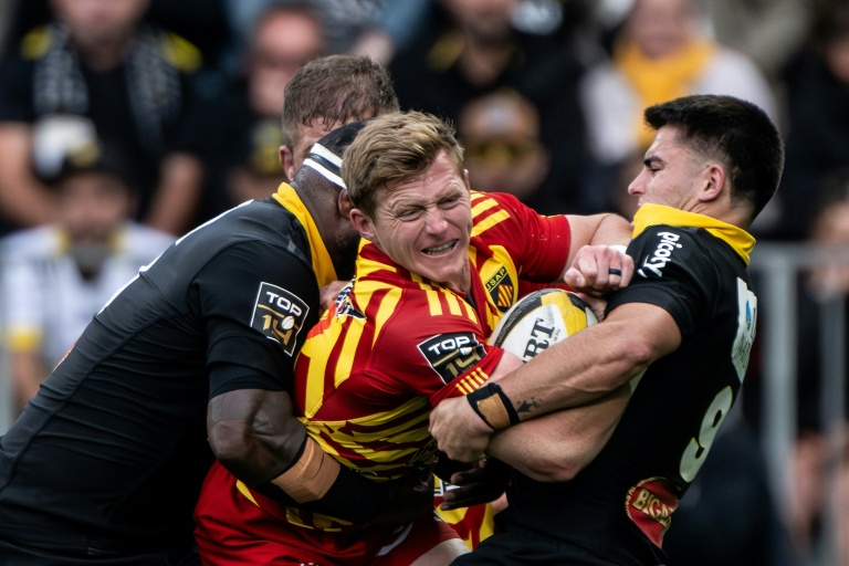 Le demi de mêlée sud-africain de Perpignan James Hall (C) tente de se frayer un chemin entre deux joueurs de La Rochelle, lors d'un match de Top 14, le 27 septembre 2025 à La Rochelle