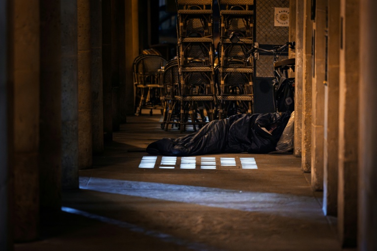 Un homme dort dans un sac de couchage à proximité d'une terrasse de café le 15 octobre 2025 à Paris