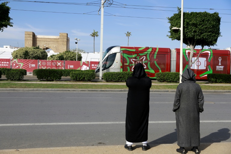 Des personnes regardent un tramway passer devant la fan zone de la Coupe d'Afrique des nations (CAN) 2025, l'une de celles prévues par la CAF, à Salé, au Maroc, le 14 décembre 2025