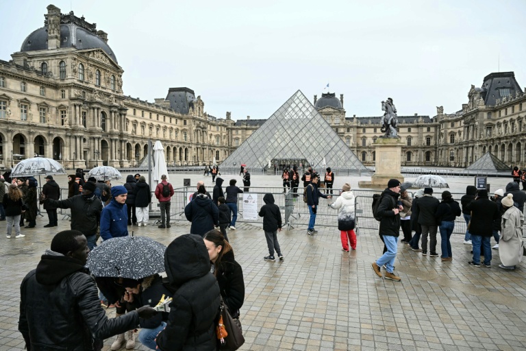 Des visiteurs devant le musée du Louvre et la pyramide conçue par l'architecte sino-américain Ieoh Ming Pei, fermés lors d'un mouvement de grève, le 12 janvier 2026 à Paris