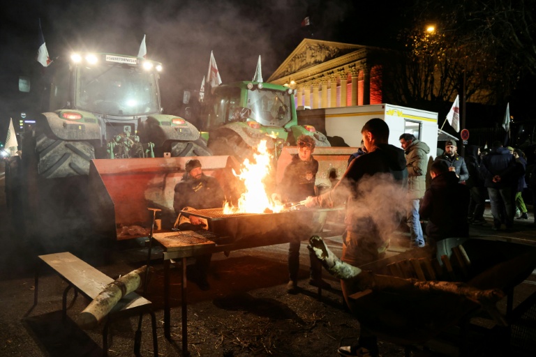 Des agriculteurs autour d'un barbecue près de leurs tracteurs garés devant l'Assemblée nationale, le 13 janvier 2026 à Paris