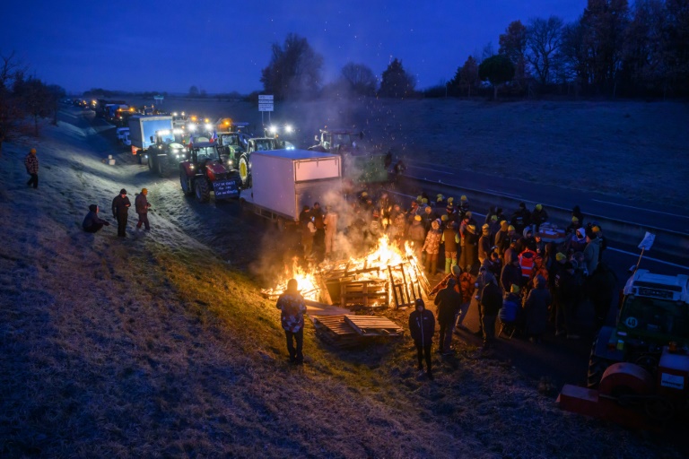 Des agriculteurs se réchauffent autour d'un feu alors qu'ils sont empêchés par les gendarmes d'entrer dans Toulouse dans le cadre de leur manifestation pour défendre leur profession et dénoncer la gestion de la crise agricole par le gouvernement, près de Leguevin, le 7 janvier 2026.