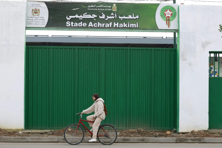 Une femme fait du vélo devant le terrain de football municipal nommé en l'honneur du footballeur international marocain Achraf Hakimi à Ksar El Kébir, dans le nord du Maroc, le 8 janvier 2026