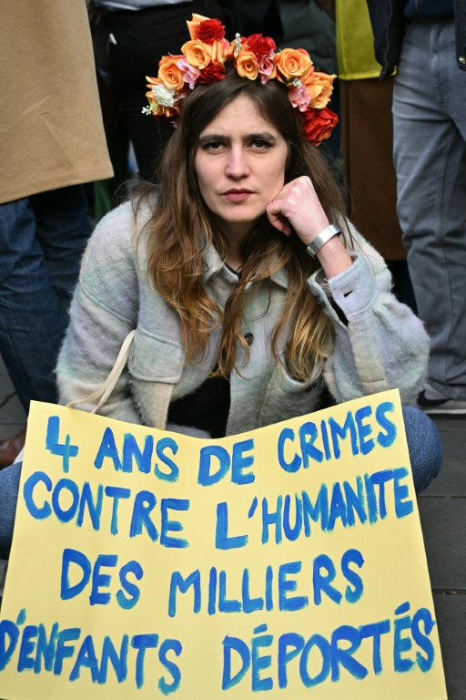 Une femme est assise derrière une pancarte où l'on peut lire « 4 ans de crimes contre l'humanité, des milliers d'enfants déportés » lors d'une marche pour l'Ukraine à Paris, à l'approche du quatrième anniversaire de l'invasion russe, le 21 février 2026