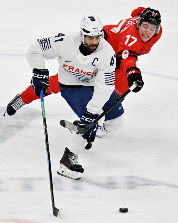 Le Français Pierre-Edouard Bellemare et le Canadien Macklin Celebrini se disputent le palet lors des JO de Milan Cortina, le 15 février 2026, à la patinoire de Milan (Italie)