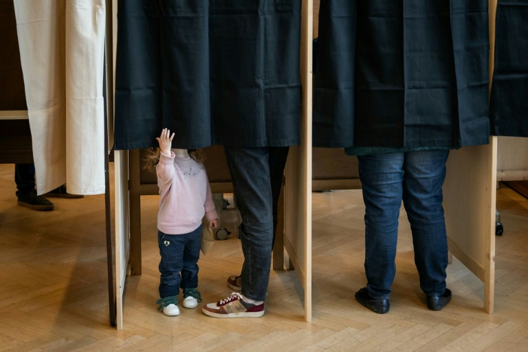 Un enfant dans l'isoloir où son père vote pour le premier tour des municipales, le 15 mars 2026 à Lyon