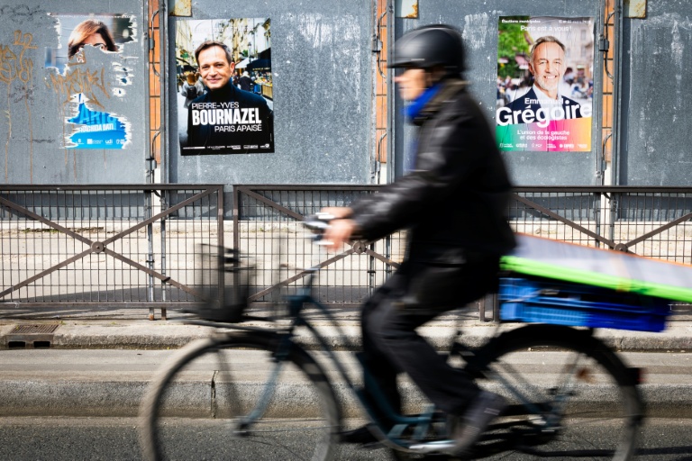 Un cycliste passe devant un panneau électoral avec les candidats à la mairie de Paris, le 7 mars 2026, à Paris
