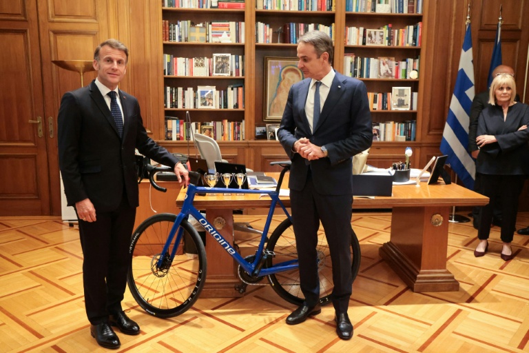Le président français Emmanuel Macron (G) offre un vélo produit en France au Premier ministre grec Kyriakos Mitsotakis à l'issue d'un déjeuner de travail, le 25 avril 2026 à Athènes