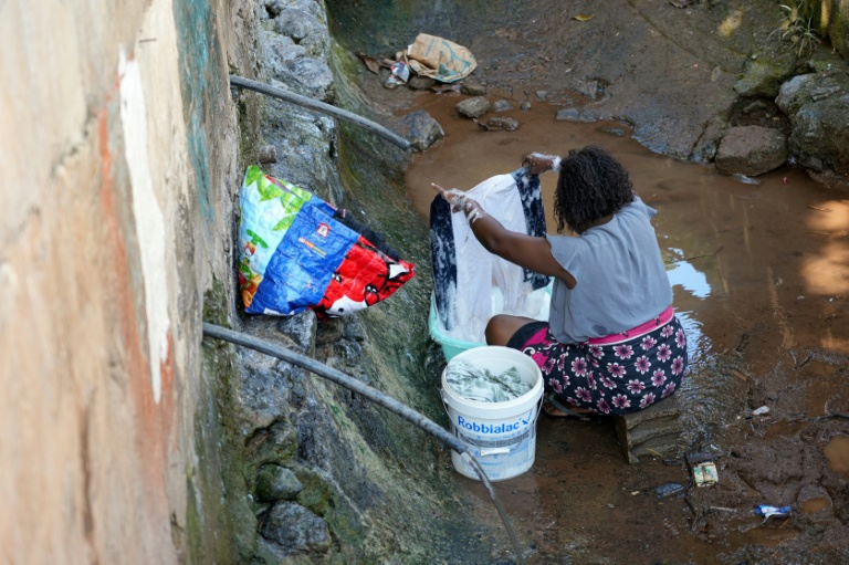 Une femme lave des vêtements à une fontaine publique distribuant de l'eau non potable à Cavani, un bidonville de Mamoudzou, le 31 octobre 2025 à Mayotte
