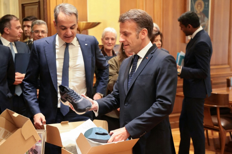 Le président français Emmanuel Macron (D) reçoit des mains du Premier ministre grec Kyriakos Mitsotakis une paire de baskets fabriquées en Grèce à l'issue d'un déjeuner  Athènes, le 25 avril 2026 à Athènes