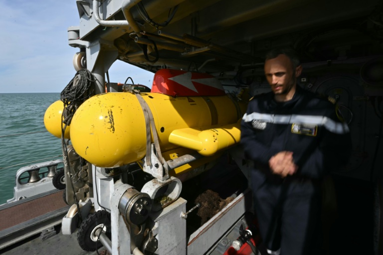 Le capitaine de corvette Jacquelin du Réau, commandant du chasseur de mines L'Aigle, à c^^oté d'un robot sous-marin jaune de déminag esur le pont du navire, au large de Dieppe, le 14 avril 2026 en Normandie