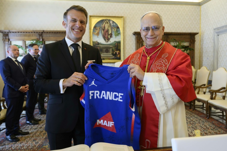 Photo prise et diffusée le 10 avril 2026 par Vatican Media montrant le président français Emmanuel Macron (g) offrant au pape Léon XIV, passionné de sport, un maillot dédicacé de l'équipe de France de basket-ball lors d'une audience privée au Vatican