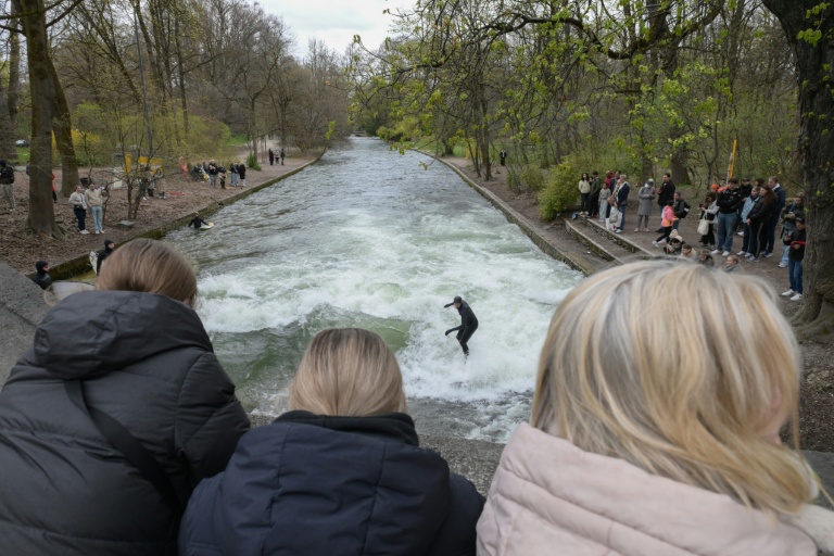 Des passants regardent des surfeurs revenir sur la vague de l'Eisbach à Munich, dans le sud de l'Allemagne, le 4 avril 2026