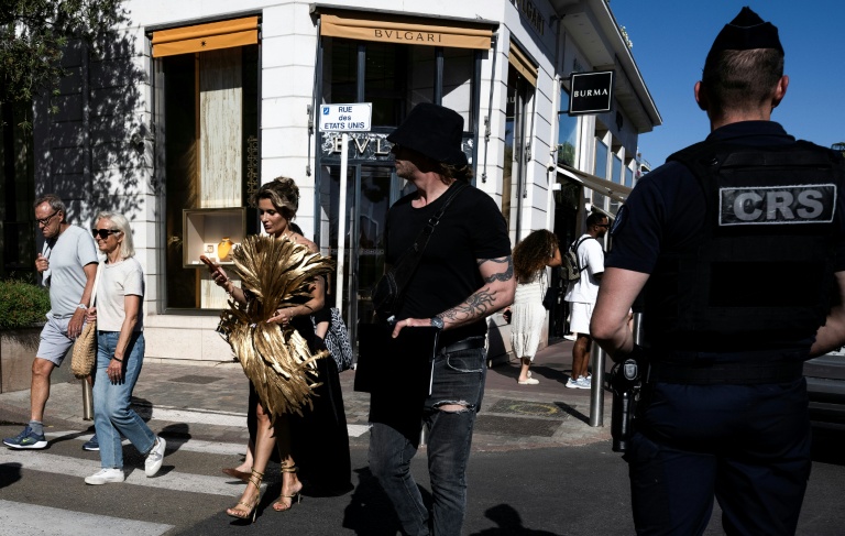 Une femme en tenue de soirée passe à côté d'un CRS en marge de la 79e édition du Festival de Cannes, le 12 mai 2026
