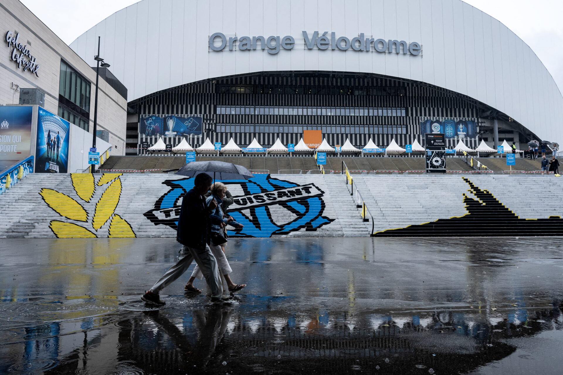 Pedestrians walk past the Velodrome Stadium on a rainy day in Marseille, southern France on September 21, 2025. The French L1 football match between Olympique de Marseille and Paris SG, scheduled for September 21, 2025 evening, has been postponed due to severe weather expected in Marseille, the Prefect of Bouches-du-Rhone announced to AFP.