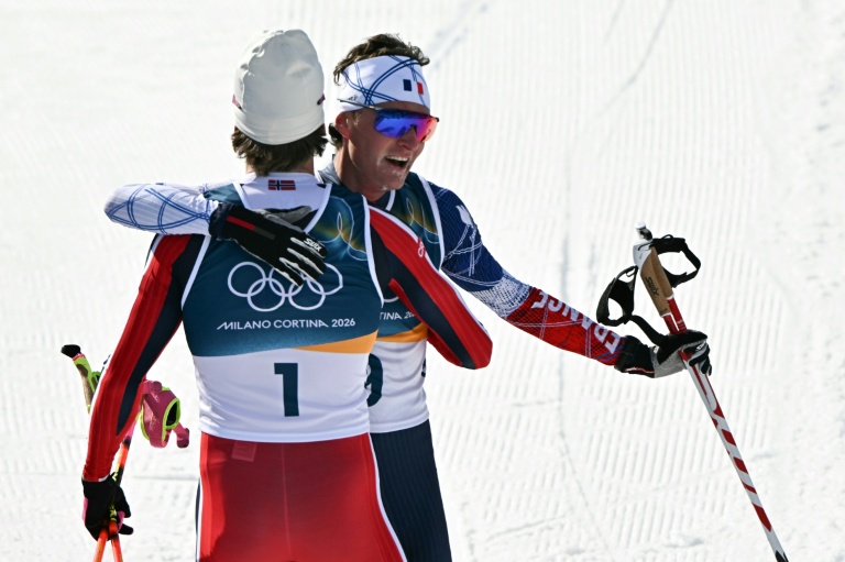 Johannes Klaebo (de dos) et Mathis Desloges à l'arrivée du skiathlon des Jeux olympiques de Milan Cortina, le 8 février 2026 à Lago di Tesero