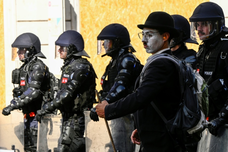 Un homme grimé en Charlie Chaplin à côté de policiers suisses en tenue antiémeute lors d'un rassemblement de la coalition 