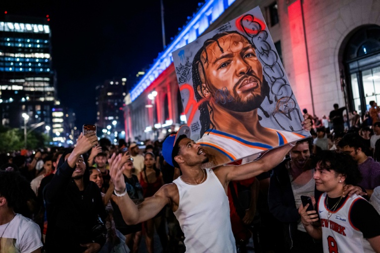 Dans les rues de New York, des fans des Knicks brandissent une pancarte à l'effigie de leur meneur Jalen Brunson, après le titre remporté au terme du match 5 des finales NBA, samedi 13 juin 2026